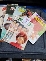 Photo showing seven vintage Mad Magazines from different years stacked with visible covers and titles.
