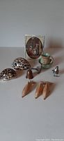 Miniature collectibles including three wooden dolphins, two spotted shells, a small cloisonné bell, tiny ceramic cup and saucer, a metal bell, a mini framed print, and a silver figurine.