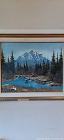 Framed oil on canvas painting showing full mountainous landscape with river and trees