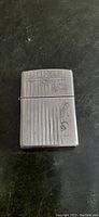 Front side of silver plated Zippo lighter with vertical stripes and floral engraving.