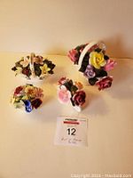 Four Staffordshire Royal Castle china flower figurines arranged on table including small baskets and floral bunches