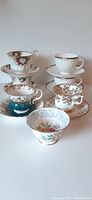 Full set of five teacups and five matching saucers arranged in a group showing various floral and gold patterned designs.