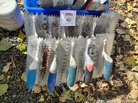 Trowels arranged side by side showing plastic handles in blue, black, pink, and white with notched metal blades from smaller to larger sizes.