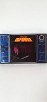 Full front view of the handheld Defender arcade game showing screen and control panels on left and right sides.