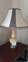 Full view of vintage handblown glass lamp showing the yellow-beige rounded base and newer fabric shade with beaded fringe.