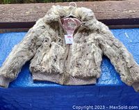 Front view of rabbit fur bomber jacket laid flat on blue surface, showing zipper front, knit cuffs and waistband, and fur texture.