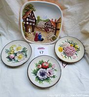 Overview photo of three handpainted chalkware wall plaques showing one village scene and two floral designs.