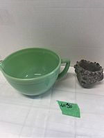 Front view of the green FireKing jadeite batter bowl with handle and spout next to a small sculpted flower pot.