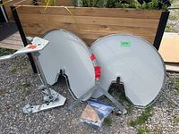 Two kidney-shaped grey lazy Susan trays shown with metal mounting brackets assembled underneath, all placed on outdoor gravel surface near wooden divider.