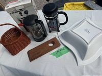 Photo showing two Bodum coffee presses, one in original box, wooden wine bottle holder, small woven basket, and La Sera serving bowl arranged on table.