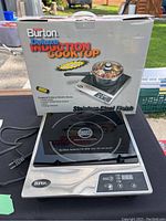 Photo of the boxed Burton Deluxe Induction Cooktop showing branding, wattage (1800W), touchscreen features, and stainless steel finish.