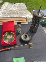 Full lot showing cloisonné plate in red box, cloisonné pen holder, brass candle holder, and brass candle snuffer on an outdoor table