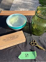 The lot displayed outside on a black cloth showing blue and white bowl, green glass pitcher, pencil ruler box, and brass snuffer
