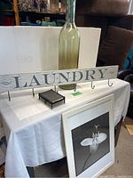 Photo of the smokey glass bottle, laundry sign with hooks, flower print, and nail impression office toy on a white tablecloth.