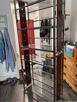 Full view of tall shelving unit showing multiple clear tempered glass shelves supported by chrome frame and brown vertical panels with circular cutouts.