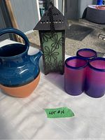 Three purple to pink gradient Mexican style drinking glasses and black metal outdoor candle holder with green floral glass panels