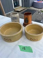 Two yellow-beige vintage dog bowls marked with 'DOG', a ceramic German beer stein, and a copper Navy Marine beer stein on a white table.