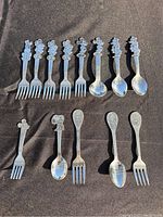 Full view of the children's stainless steel cutlery with Disney character handles, including forks and spoons, all laid on a dark background.