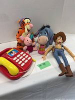 Lot including Tigger, Piglet, Eeyore plush toys, Woody figure, Mickey Mouse phone on white background