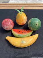 Five vintage hand carved stone fruit pieces arranged on black cloth, showing natural marble/onyx textures and shape details.