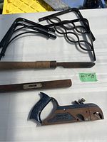 Photo showing four black metal ornate shelf brackets, large carving tool with wooden handle, wooden spirit level, and Stanley hand planer with wooden handle and blue metal body