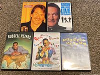 Photo showing all 5 DVDs arranged on carpet, featuring front covers of Jeff Foxworthy, Robin Williams, and three Russell Peters DVDs.
