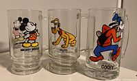 Front view of three Disney glass mugs featuring Mickey Mouse, Pluto, and Goofy.