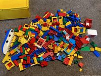 Photo of a large pile of colorful Lego Duplo blocks spilling from a yellow container, including various pieces and a boat hull.
