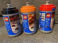 Three LEGO Sports hockey player sets in cylindrical cases with blue, orange, and red lids indicating sets 3543, 3541, and 3540.