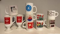 Group photo of all 10 milk glass mugs showing variety of prints and designs including Kodak, Peek Freans, Scouts Jamboree, tulip flowers, and Love Grandpa.