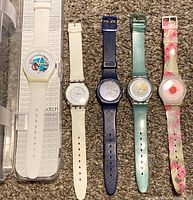 Five Swatch watches laid out, showing their bands and faces for identification and condition overview