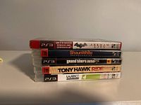 Stack of five PS3 game cases showing titles and conditions, Batman Arkham City sealed but wrapper torn.