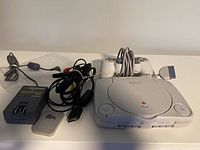PlayStation One Slim console with wired controller and all cables laid out.