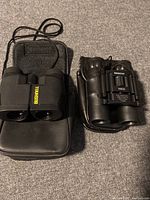 Both binoculars and their carrying cases displayed side by side on carpeted floor