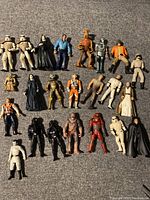 Top-down view showing all 23 Star Wars action figures arranged on a grey carpeted surface, displaying the full lot.