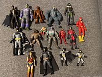 All 16 superhero action figures arranged side by side on a gray fabric surface. Includes multiple Batman figures, Hulk, Flash, and others.