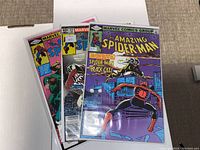 Photo showing three comic books in protective sleeves, partially overlapping, with visible cover art from The Amazing Spider-Man #231 featuring Spider-Man and Black Cat.