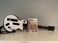 Front view of the white Gibson-style guitar controller with strap, Guitar Hero Aerosmith game case, and manuals.