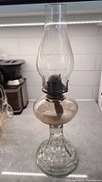 Full view of the antique pressed glass oil lamp, showing clear pressed glass base with ribbed design, clear oil reservoir, metal burner, and glass chimney.