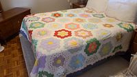 Full bed coverage showing vibrant floral patchwork quilting on top of bed with wood furniture visible in background.
