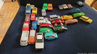 Top-down view of 26 assorted diecast cars arranged on a table, showing variety in colors and styles including sedans, wagons, and sports cars.