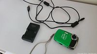 Green Fujifilm Finepix XP20 camera and black Fujifilm charger with attached cords on white surface.