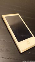 Close-up of the gold iPod Nano 7th Generation showing the front side with screen off and circular home button.