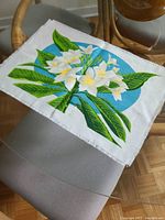 Rectangular cloth place setting with printed green leaves and white flowers, laid on glass table