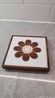 Top view of vintage wooden trivet showing painted ceramic tile with flower design
