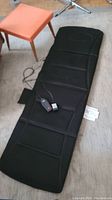 Full view of black Tony Little massage mat laid flat on floor with visible stitched sections and side pouch.
