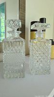Two different cut glass decanters side by side, showing intricate cut patterns and square stoppers.