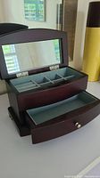 Wooden jewelry box open with hinged glass mirror and visible compartments with ring slots and sections for jewelry, walnut finish with soft interior lining, drawer opened showing fabric liner and double silver knobs.