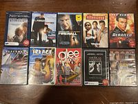 Photo showing 10 DVDs stacked in two rows including titles like Atonement, The Pursuit of Happyness, Firewall, The Hangover, Derailed, Superman Returns, Ice Age Dawn of Dinosaurs, Glee Encore, American Gangster, and Burn After Reading.