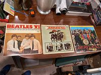 Three Beatles vinyl albums laid out on a wooden surface: Beatles VI, Beatles '65, Sgt. Pepper's Lonely Hearts Club Band